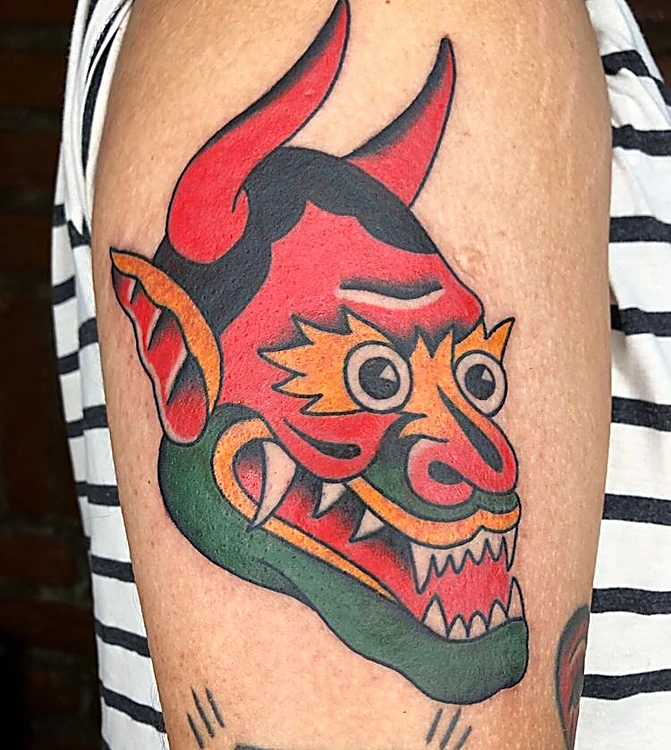 Máscara de demonio japonés en rojo, naranja y verde sobre el brazo