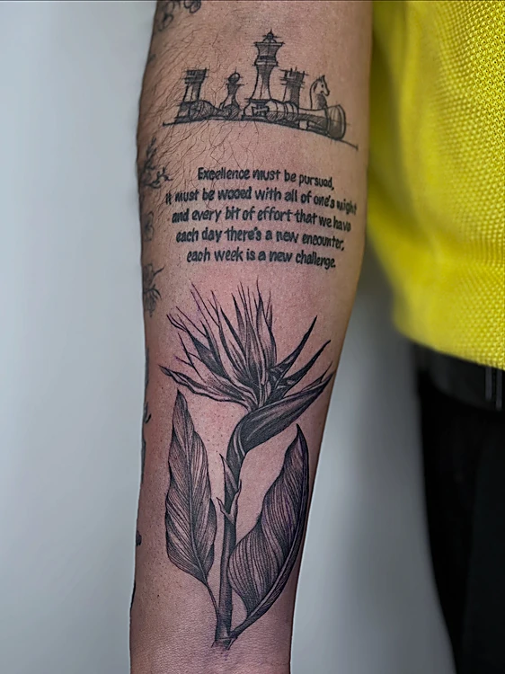 Frase en inglés con una ave del paraíso debajo, en línea negra sobre el antebrazo